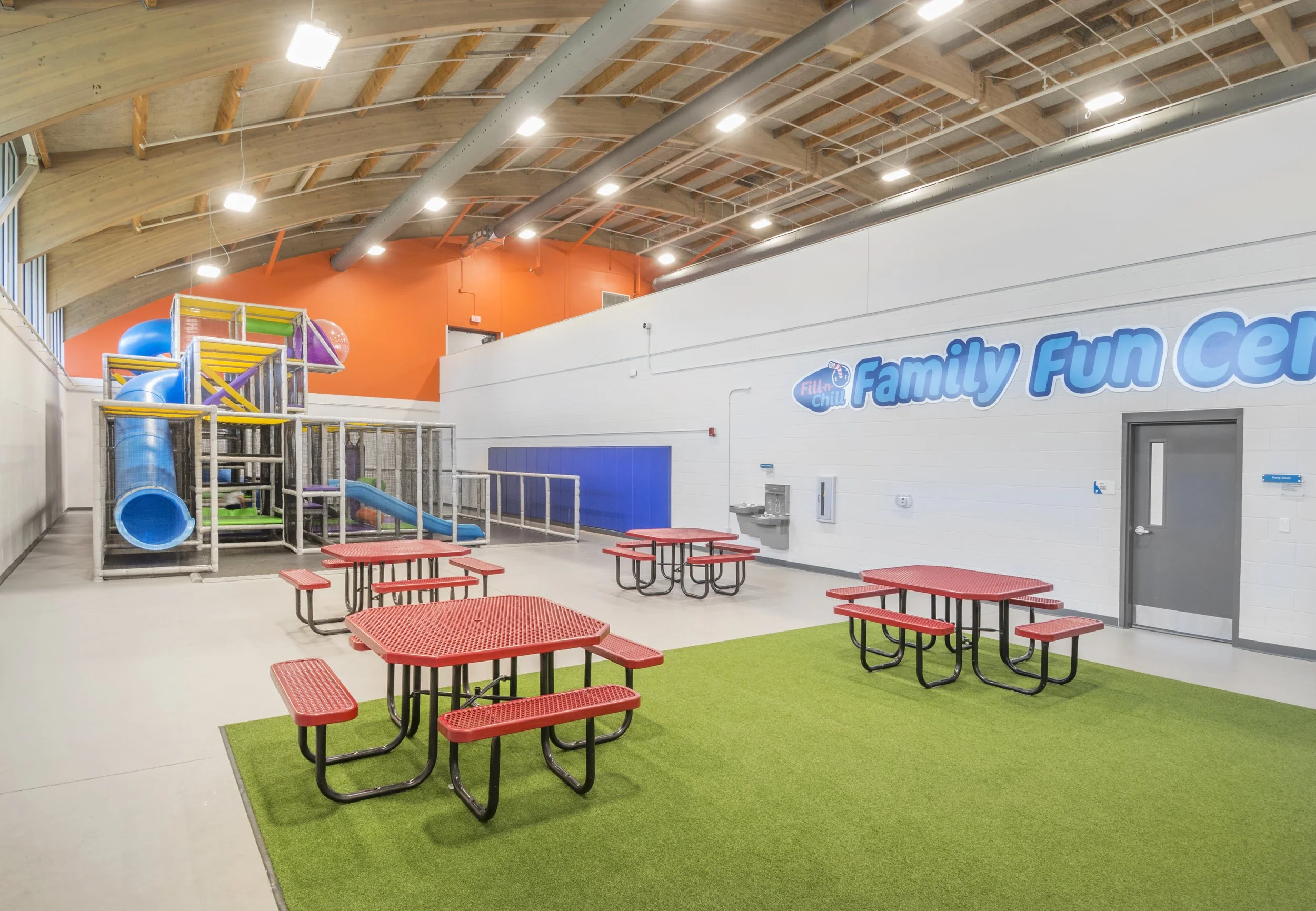 Family fun center with an indoor playground, turf floor and red picnic tables
