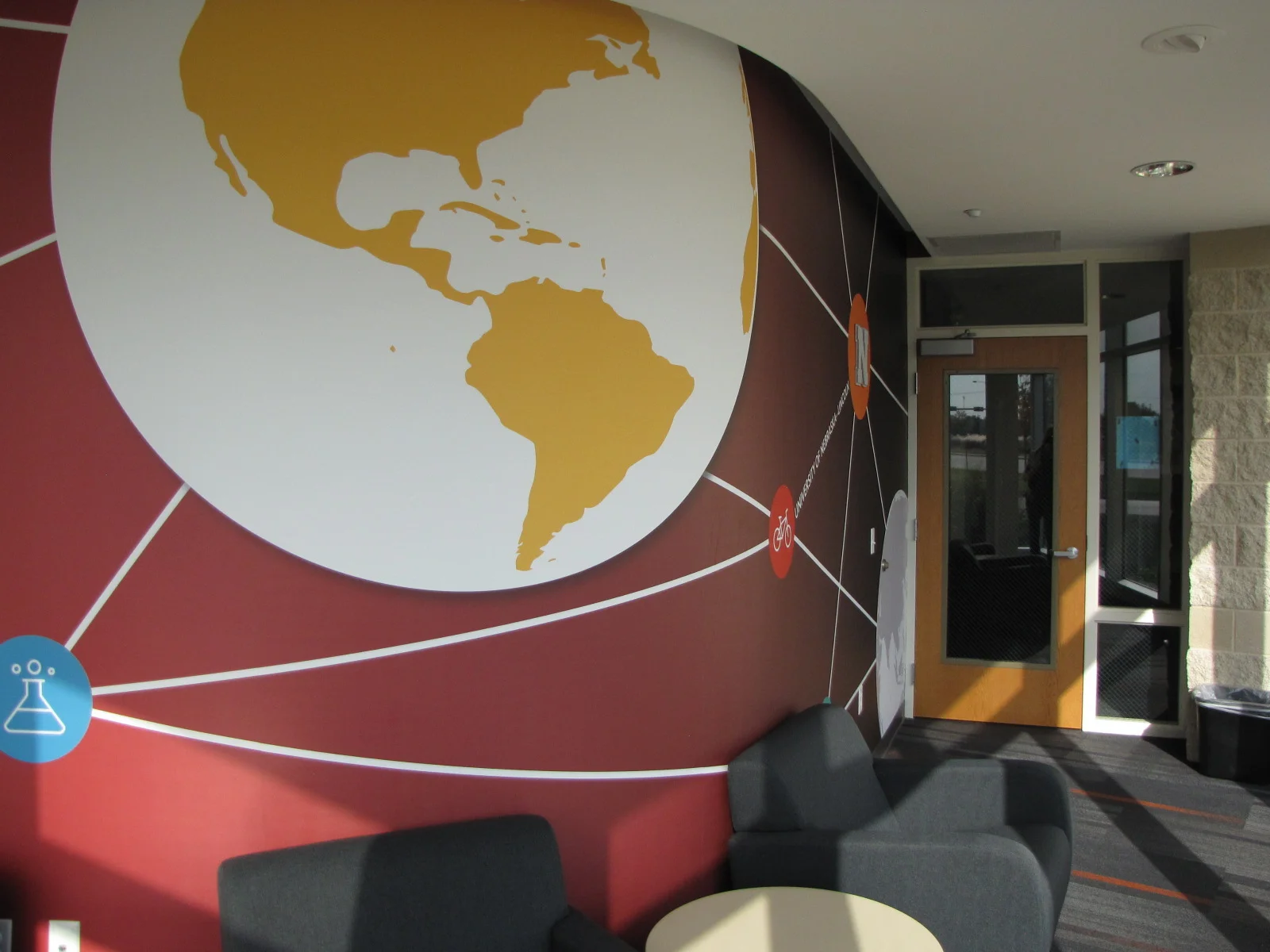 Lounge with a world map mural on a red wall and gray seating