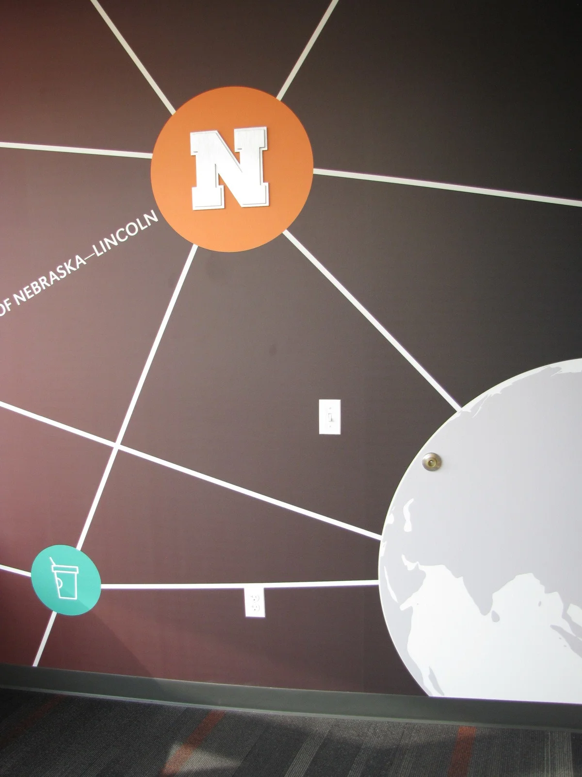 Wall graphic with a Nebraska N logo and connecting lines on a dark red wall