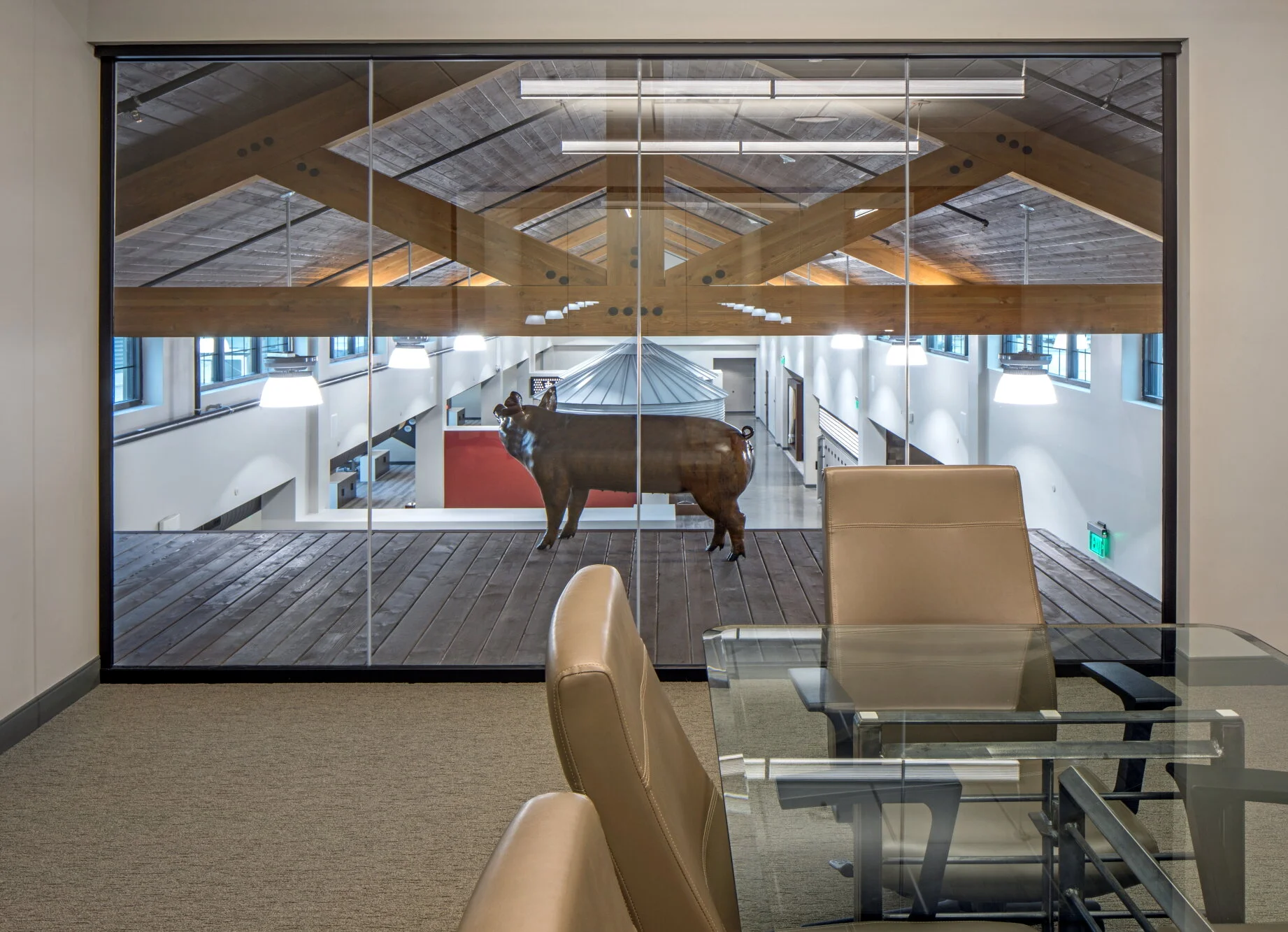 Glass-walled office with timber trusses and a bison sculpture in the atrium beyond