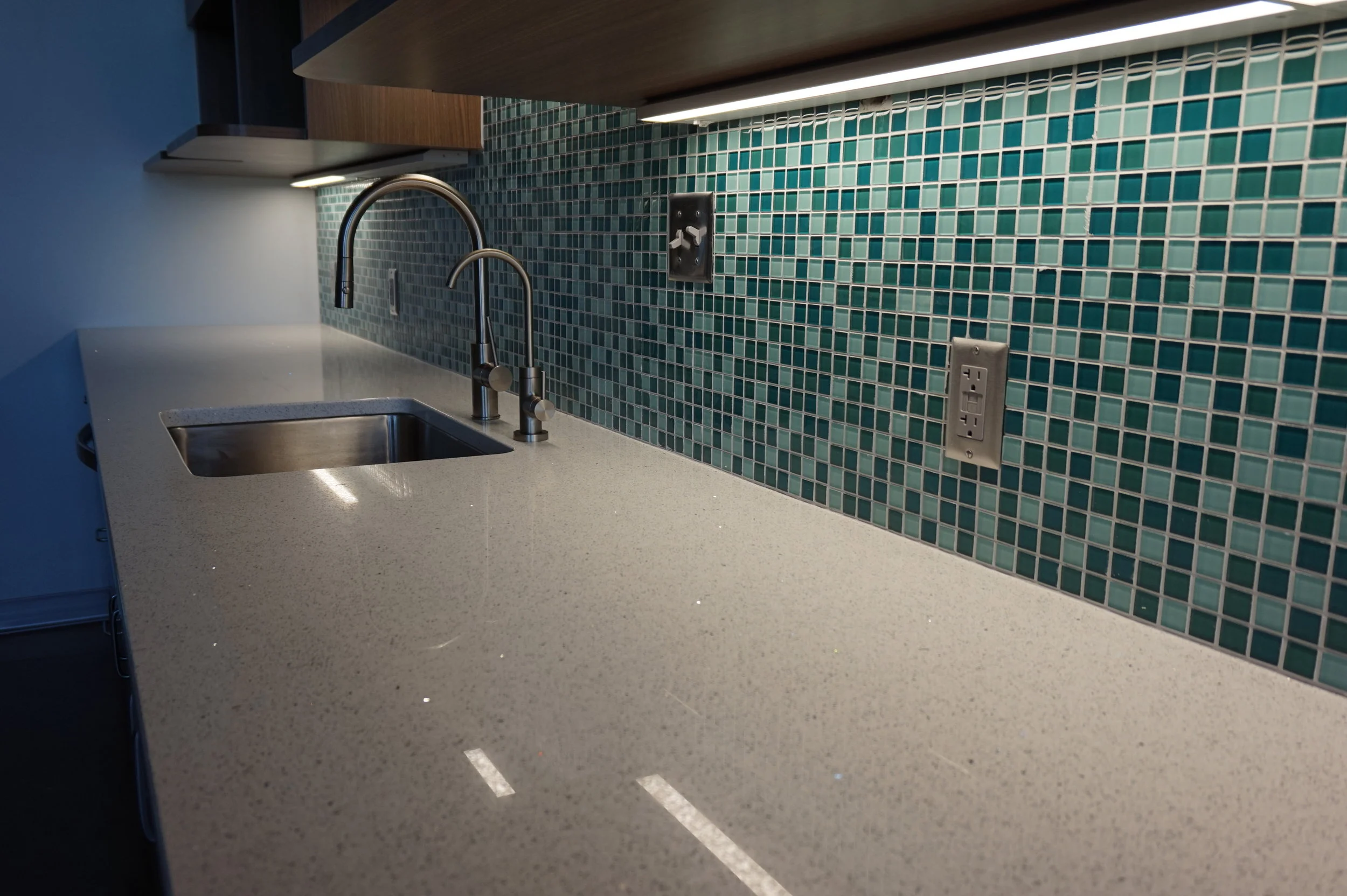 Kitchen counter with a teal mosaic tile backsplash and under-cabinet lighting