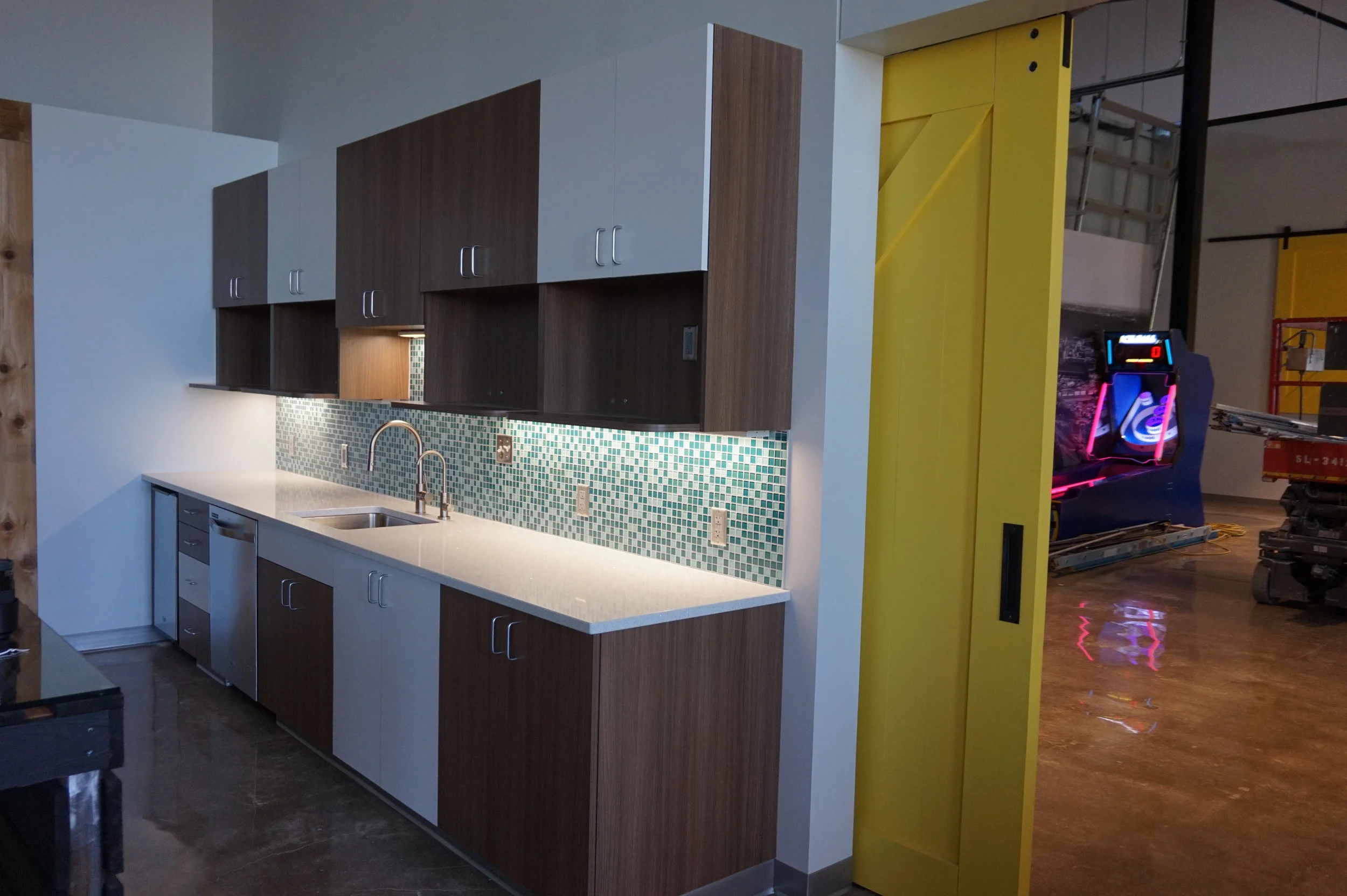 Office kitchen with wood cabinets, teal mosaic backsplash and a yellow sliding door