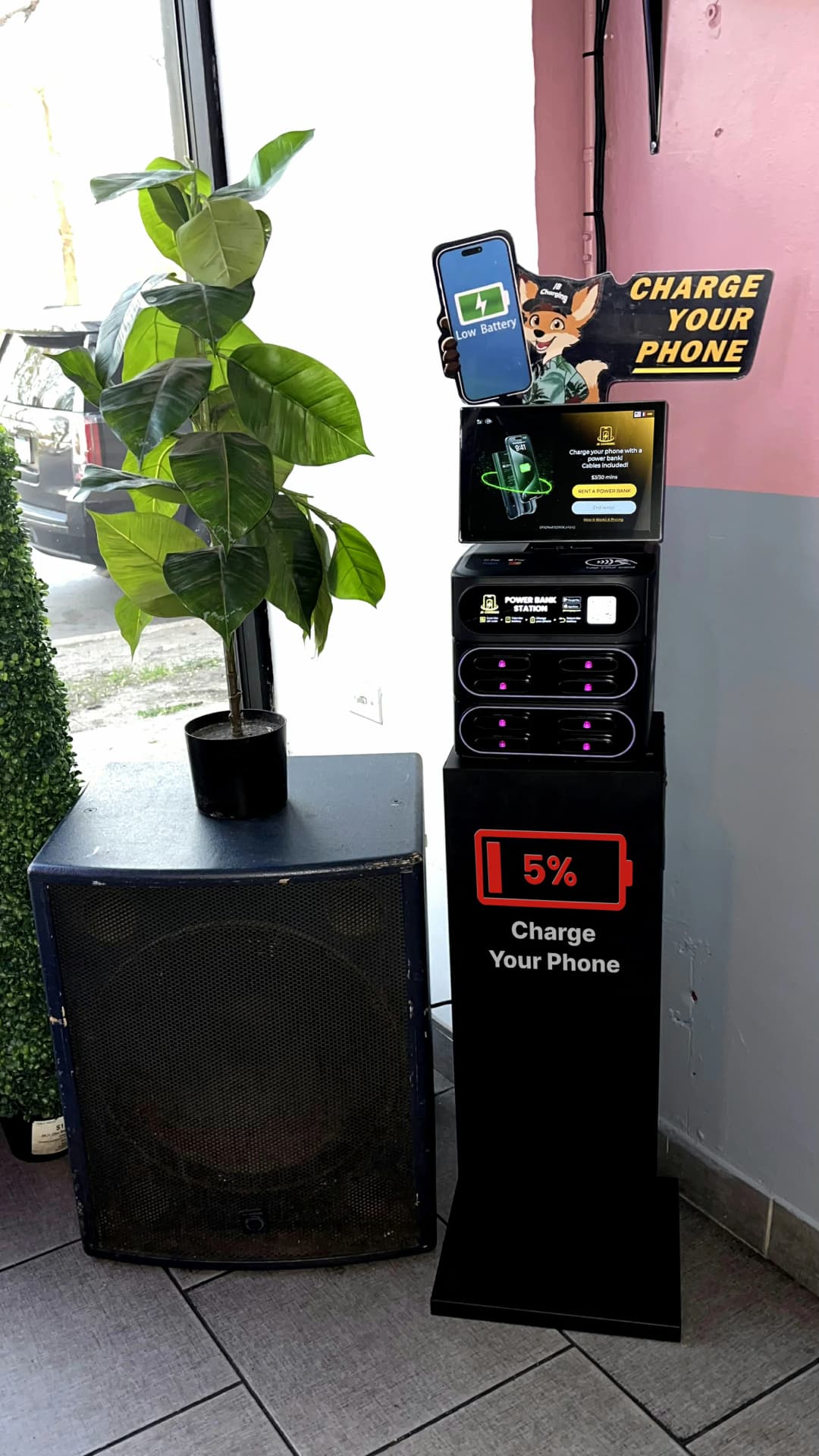 A JB Charging station on a pedestal beside a bright venue window and plant.