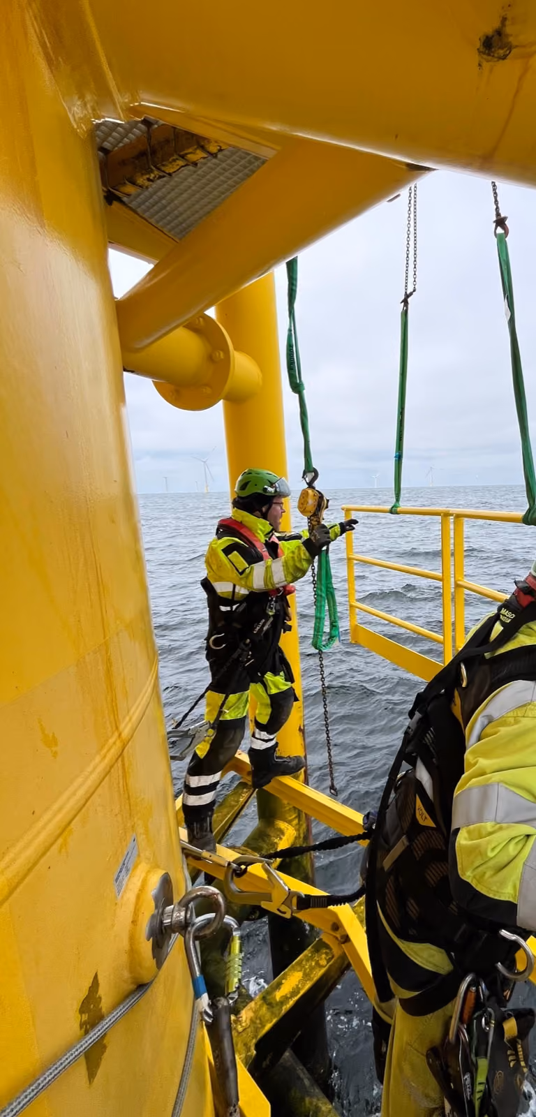 Monteur am gelben Transition Piece einer Offshore-Anlage