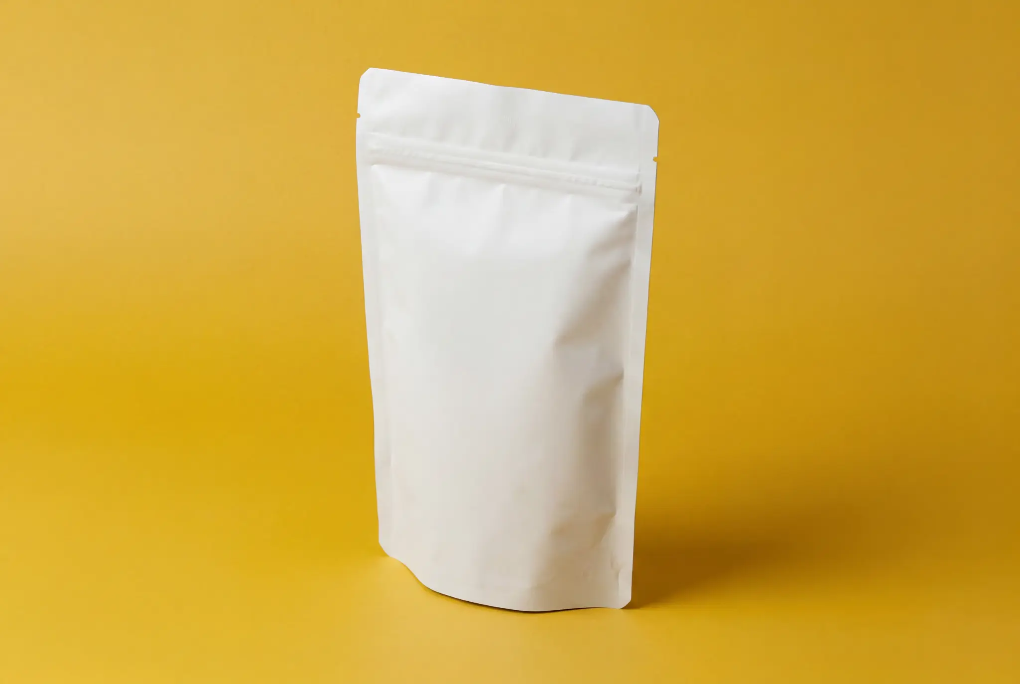 Plain white stand-up pouch on a yellow background, suitable for packaging.