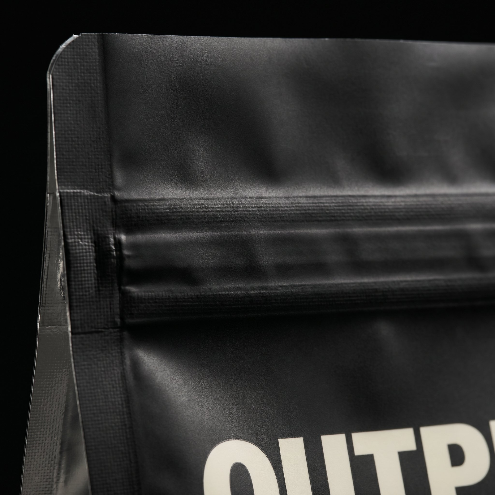 Close-up of black resealable pouch corner with visible zip lock and partial white text.