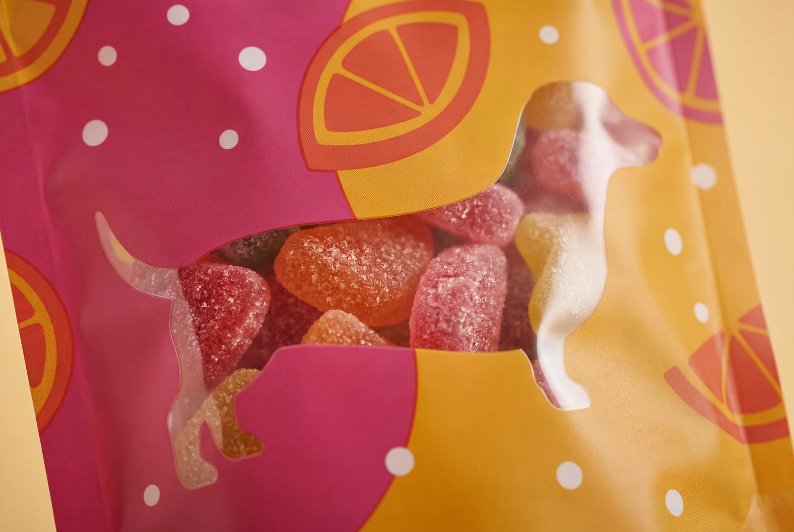 Colorful sour gummy candies seen through a clear dachshund-shaped window on packaging.