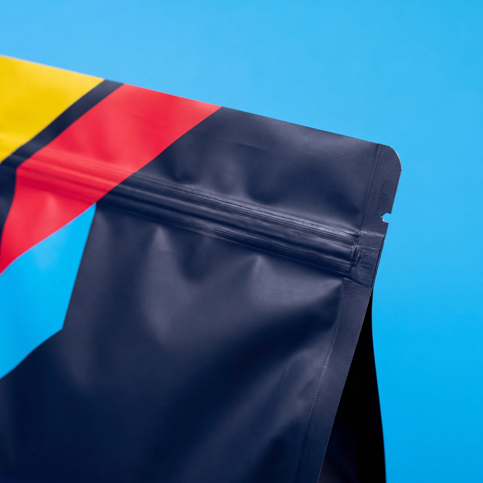 Close-up of a black resealable stand-up pouch with yellow, red, and black stripes on top.