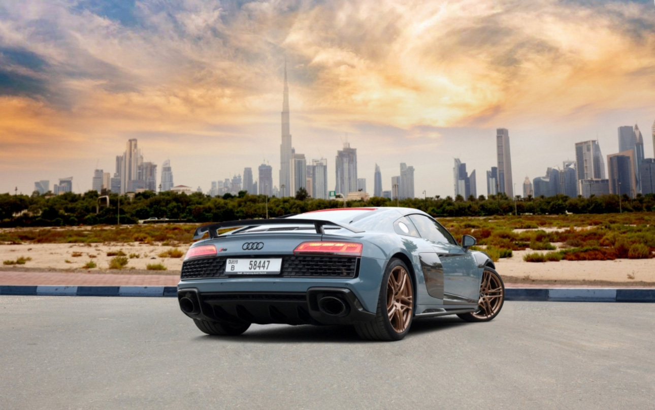 Blue Audi sports car parked with Dubai skyline and dramatic sunset backdrop
