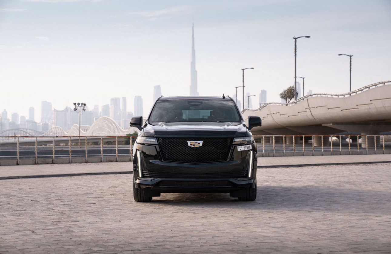 Black Cadillac SUV parked with Dubai skyline and modern bridge in background