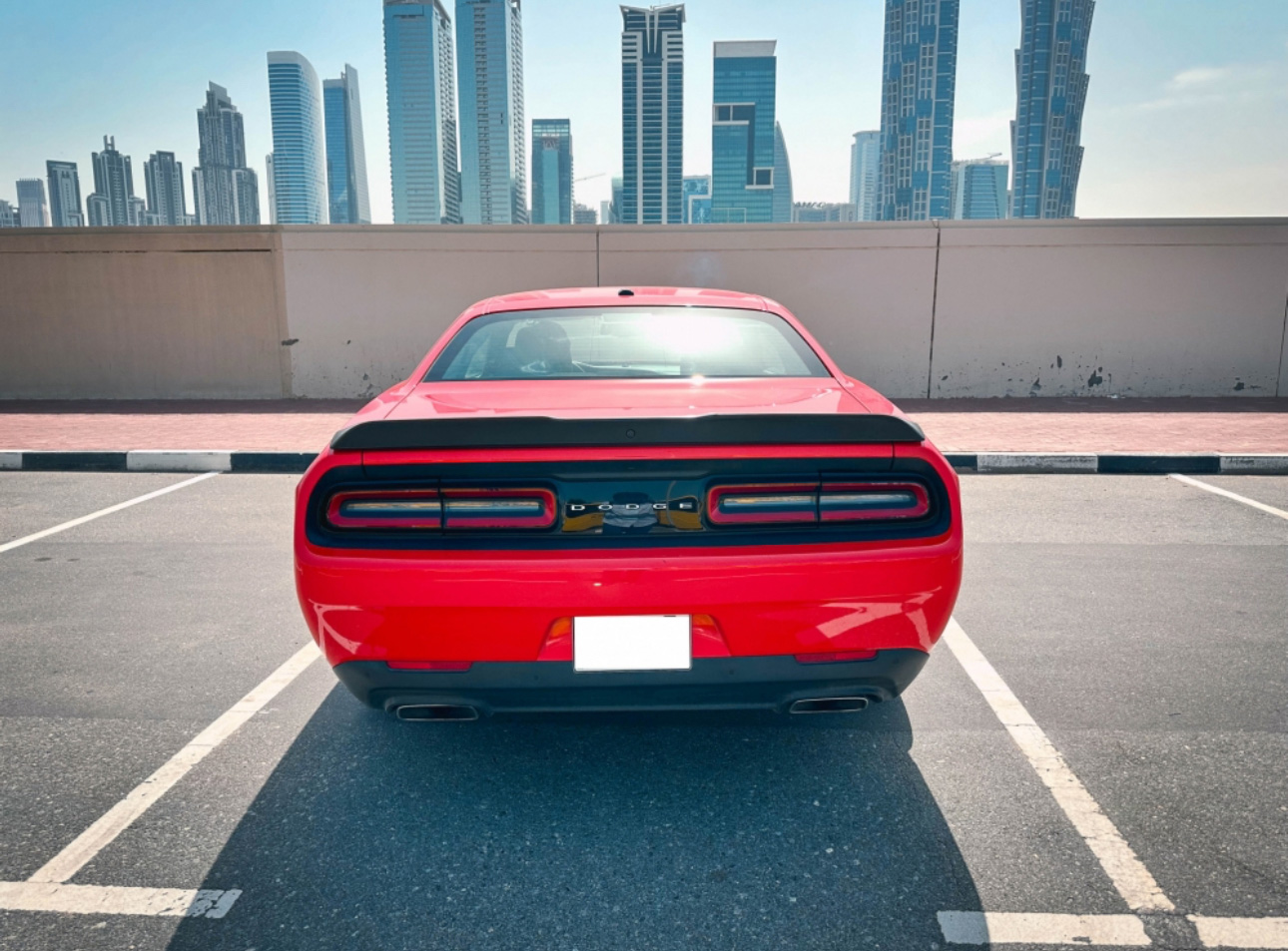 Red muscle car parked in front of Dubai skyscrapers