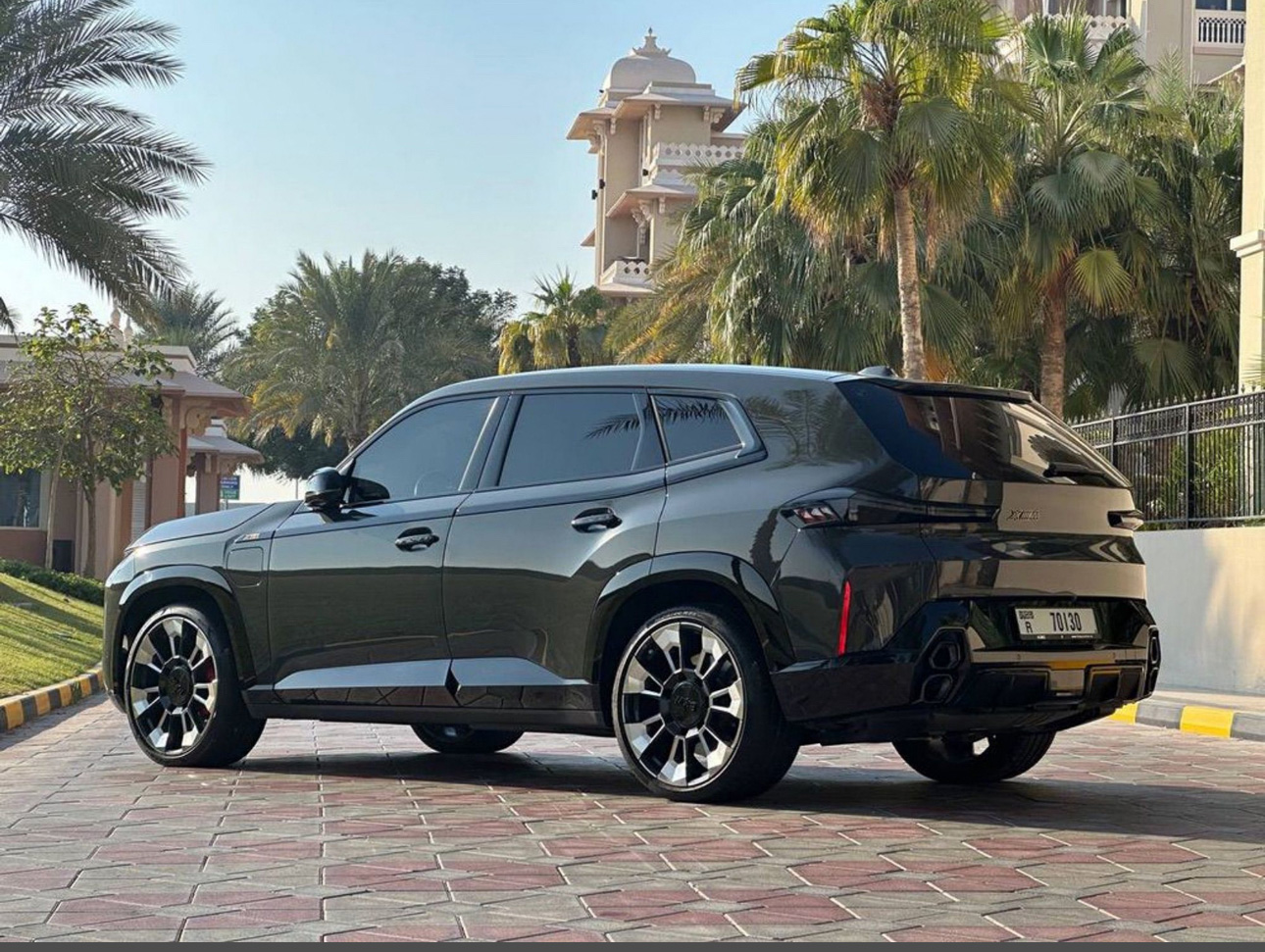 Black luxury SUV parked on tiled street with palm trees and buildings