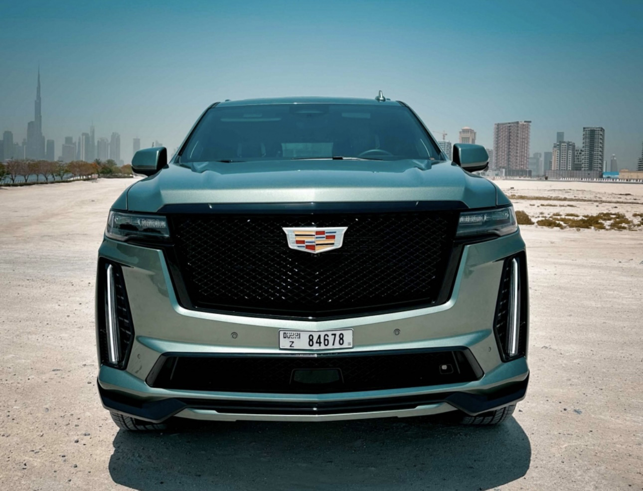 Teal Cadillac SUV parked in desert with Dubai skyline in background
