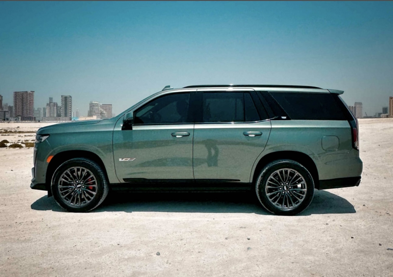 Green Cadillac Escalade SUV parked in desert with city skyline backdrop