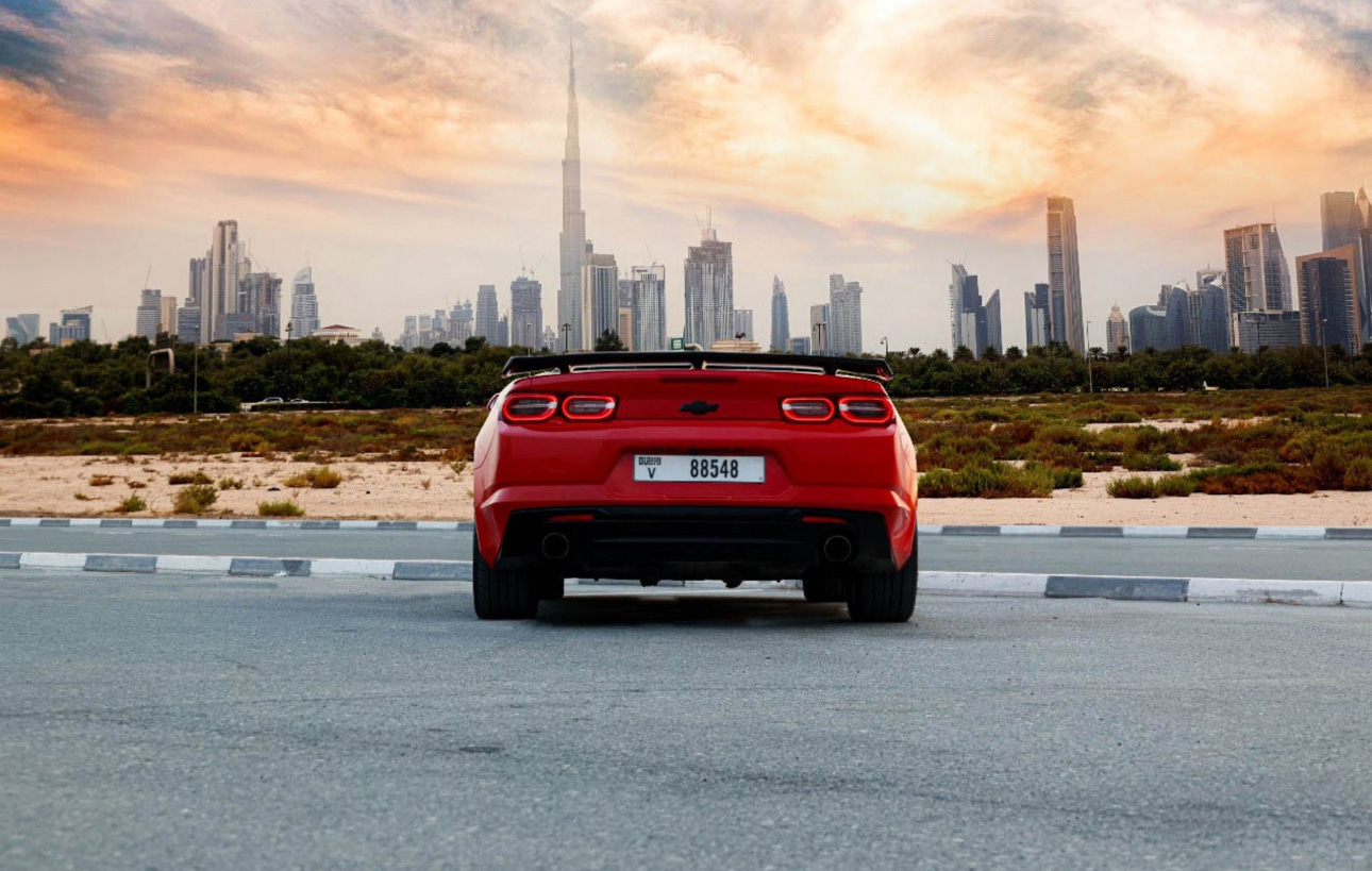Red Chevrolet sports car with Dubai skyline at sunset