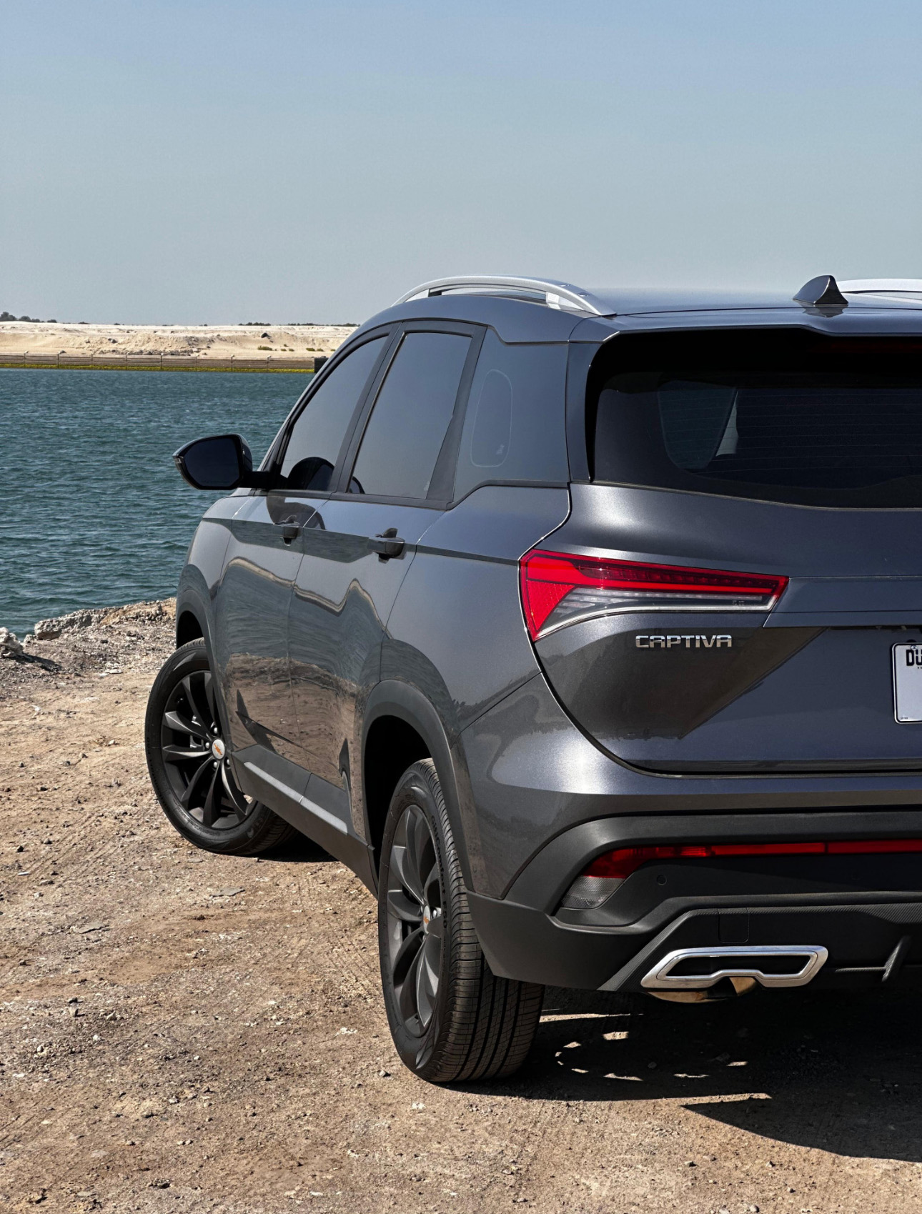Gray Chevrolet Captiva SUV parked by water with rocky shoreline