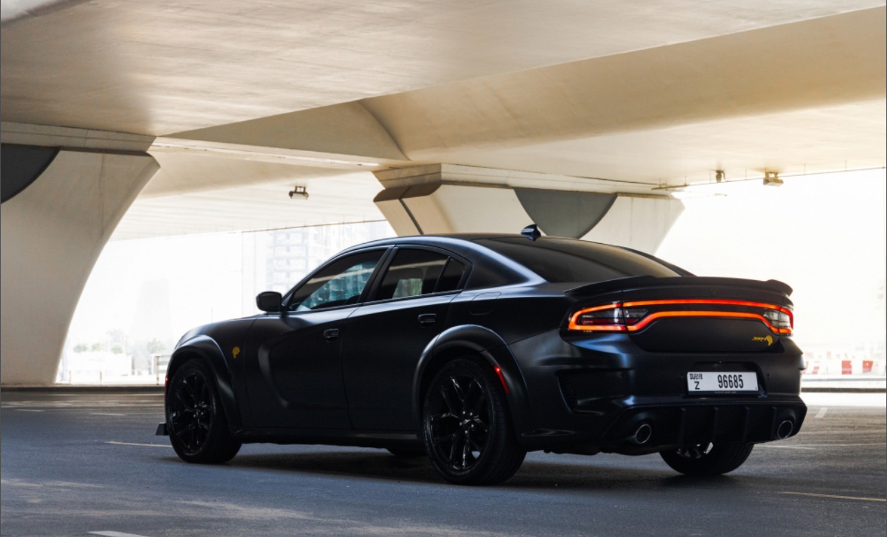 Black Dodge Charger with glowing taillights parked under concrete structure