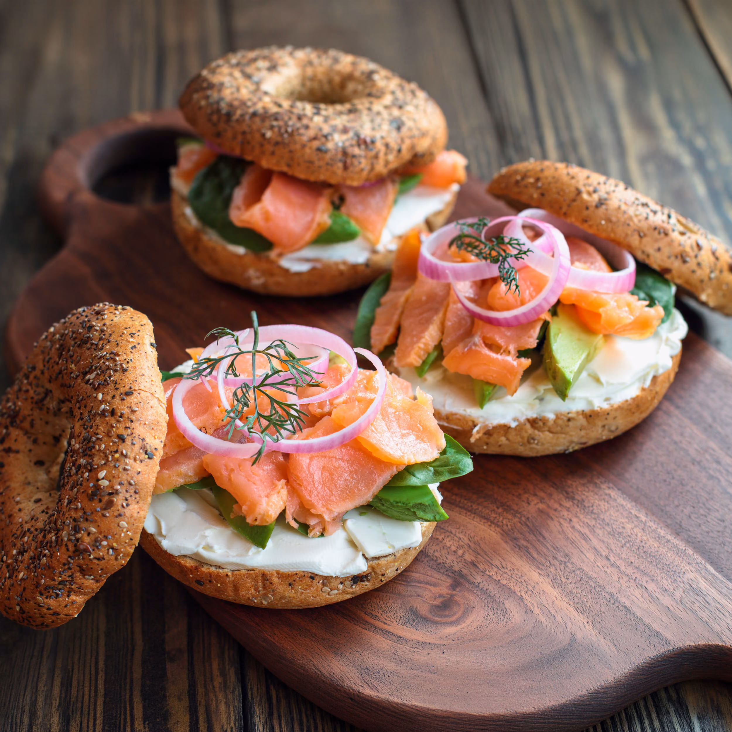 Three bagel halves with cream cheese, smoked salmon, spinach, avocado, red onion, and dill.