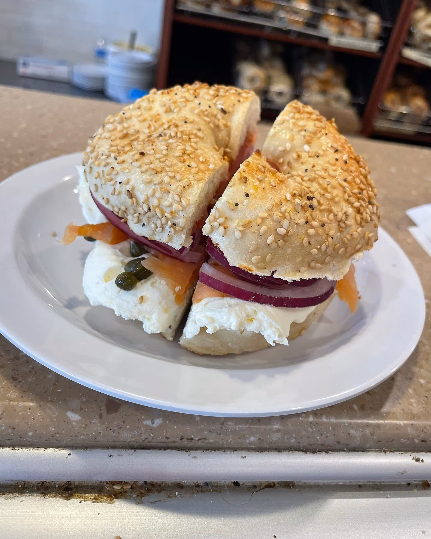 Sesame seed bagel sandwich with cream cheese, red onion slices, smoked salmon, and capers on a white plate.