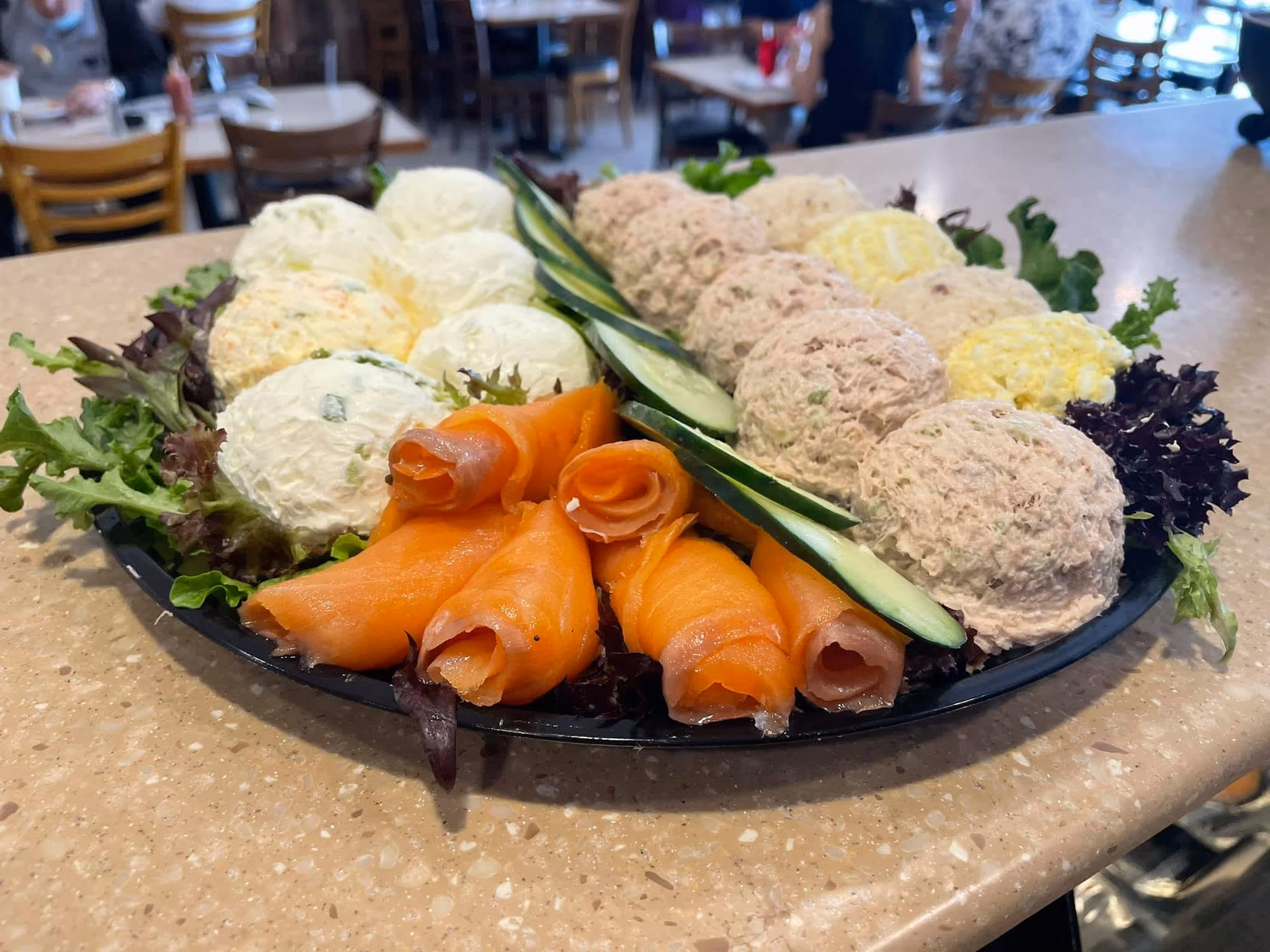 Tray of assorted spreads including smoked salmon rolls, creamy cheese balls, and sliced cucumbers on lettuce.
