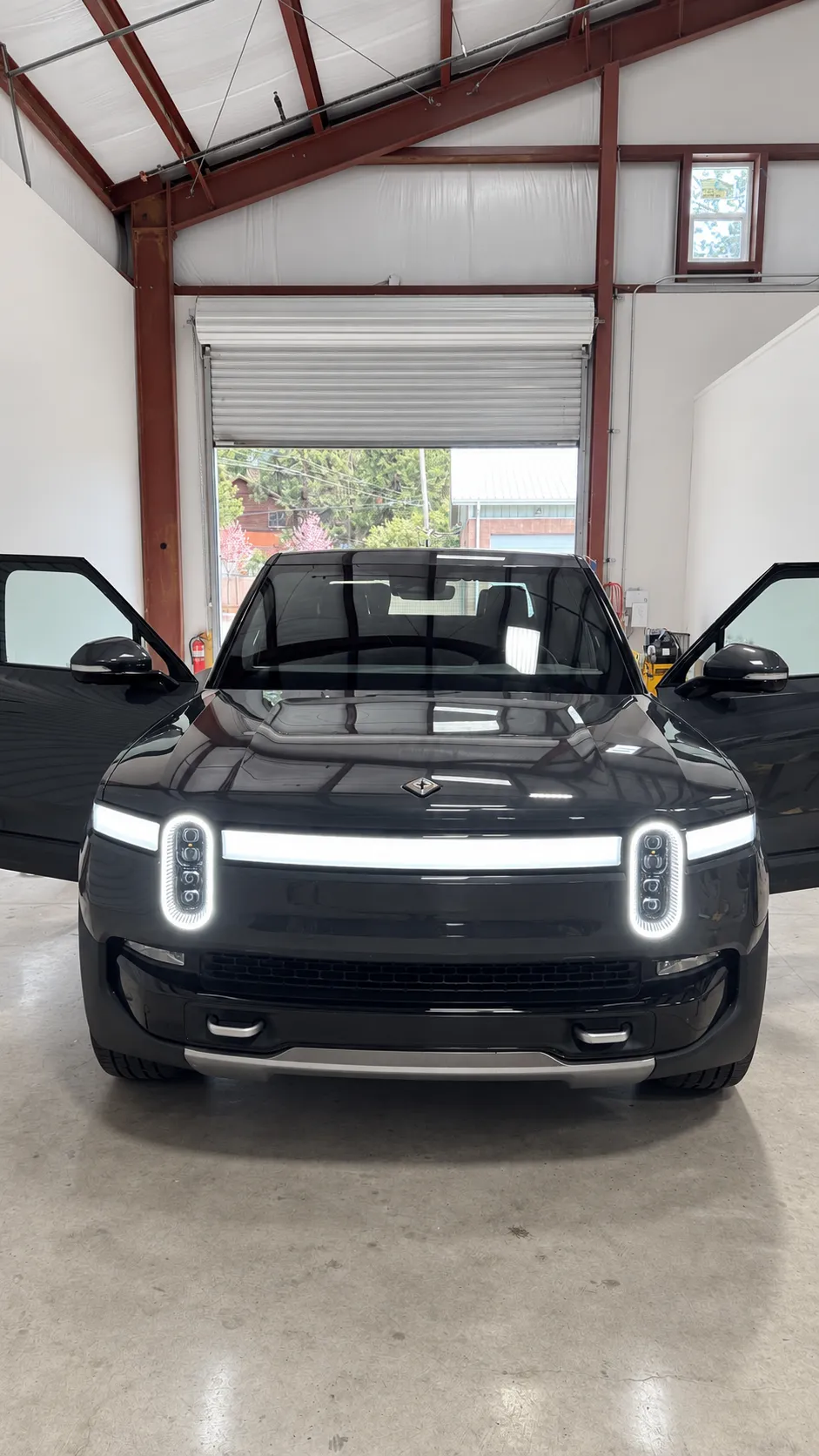 Dark Rivian with its front doors open inside the Truckee auto glass shop.