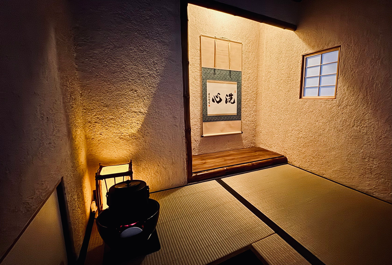 Inside the Tai-An tearoom at night: a calligraphy scroll in the alcove, a small lantern and an iron kettle on the tatami.