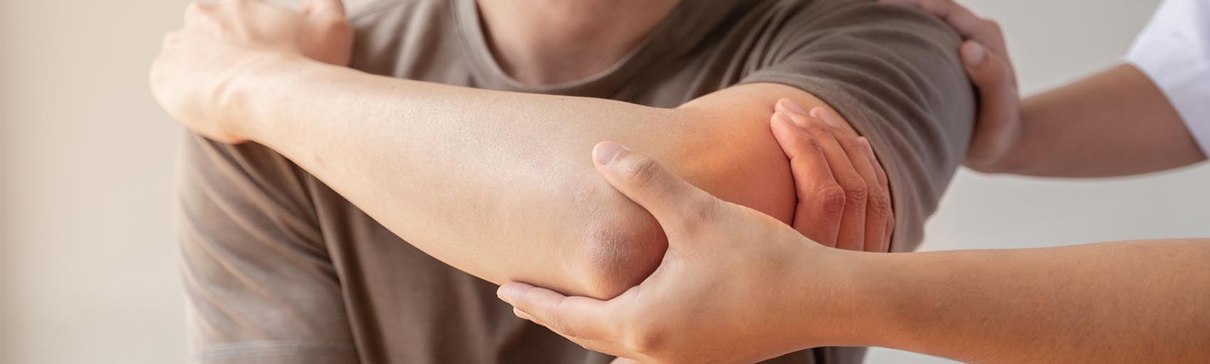 A person in a brown shirt is having their elbow carefully examined and supported by a physiotherapist's hands.