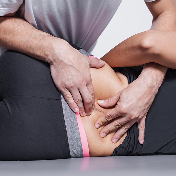 Close-up of a therapist's hands applying manual therapy to a person's lower back while the person lies on their side.