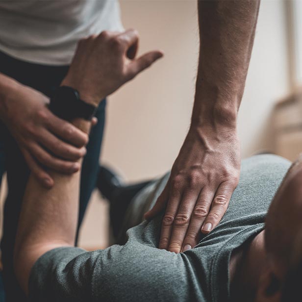 Close-up of a person receiving a shoulder massage or physical therapy, with one hand applying pressure on the shoulder and the other holding the wrist.