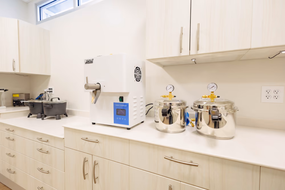 Laboratory countertop with light wood cabinets holding scientific equipment including a white cold conditioner machine and two stainless steel autoclaves with pressure gauges in a clean, well-lit room.
