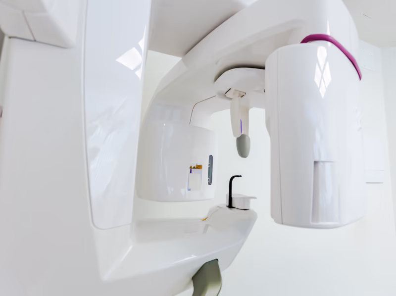 Close-up of a modern white dental X-ray machine with purple accents in a bright clinical setting.