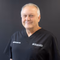 Portrait of a smiling middle-aged man wearing a black shirt with the National Health Service logo and text.