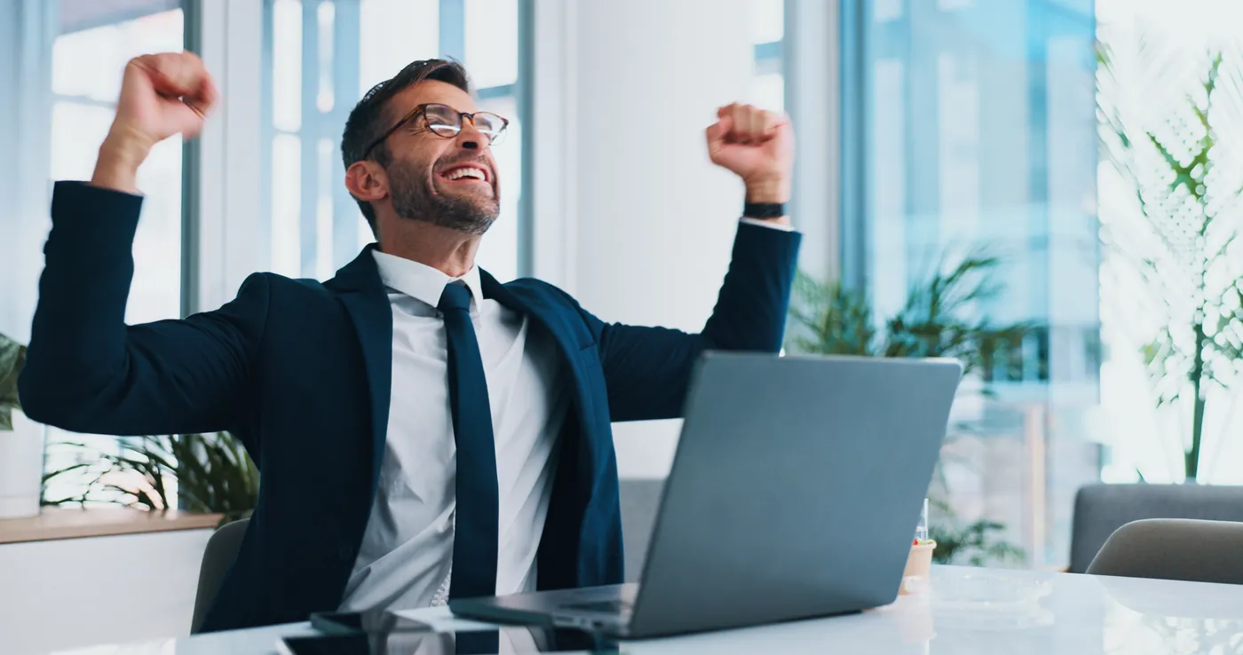 Client celebrating at his laptop, the payoff of a long-term support partnership
