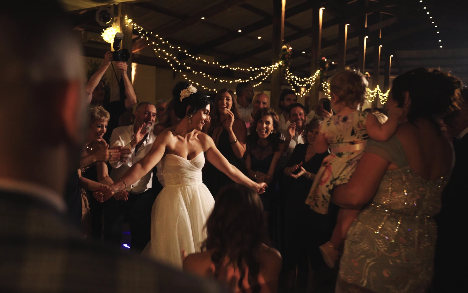 Bride dancing with guests beneath warm string lights