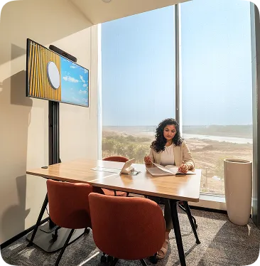 Woman reviewing documents at a conference table in a sunlit office with large windows overlooking a beach.