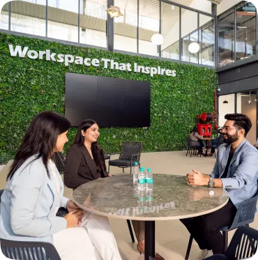 Three professionals sitting at round table in a modern workspace with green wall and sign 'Workspace That Inspires'.