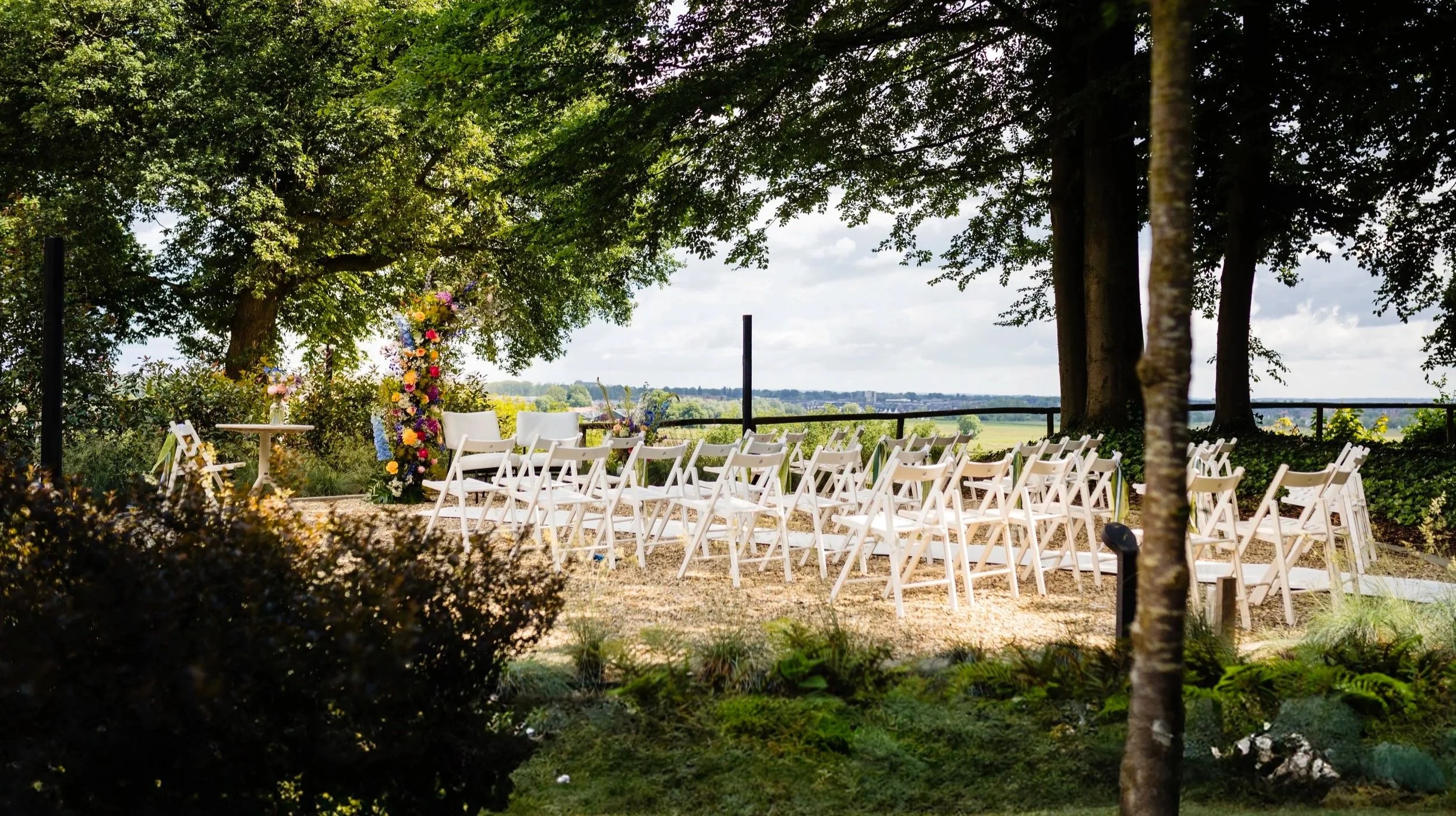 Ceremonieopstelling met witte stoelen in het groen, met uitzicht over de uiterwaarden