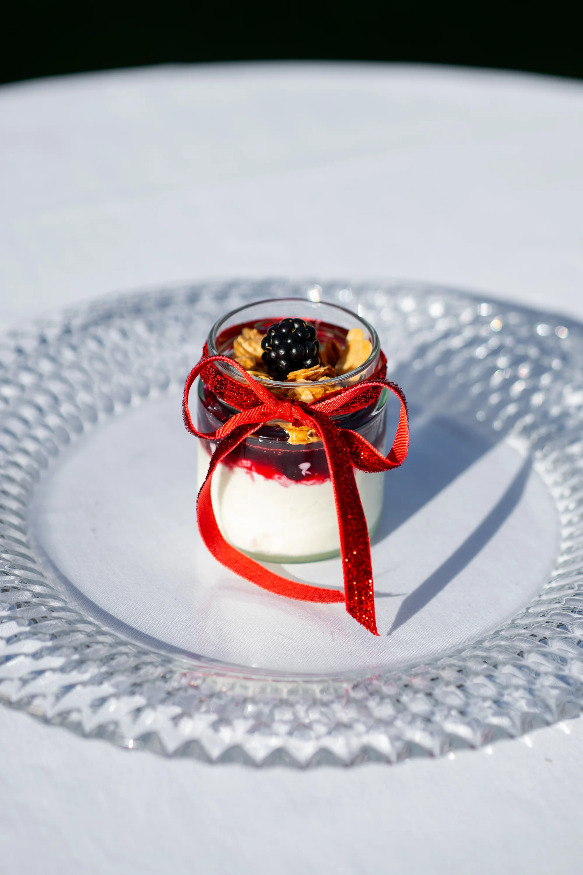 Hangop met roodfruitcompote en krokante amandel in een glaasje met rood lint