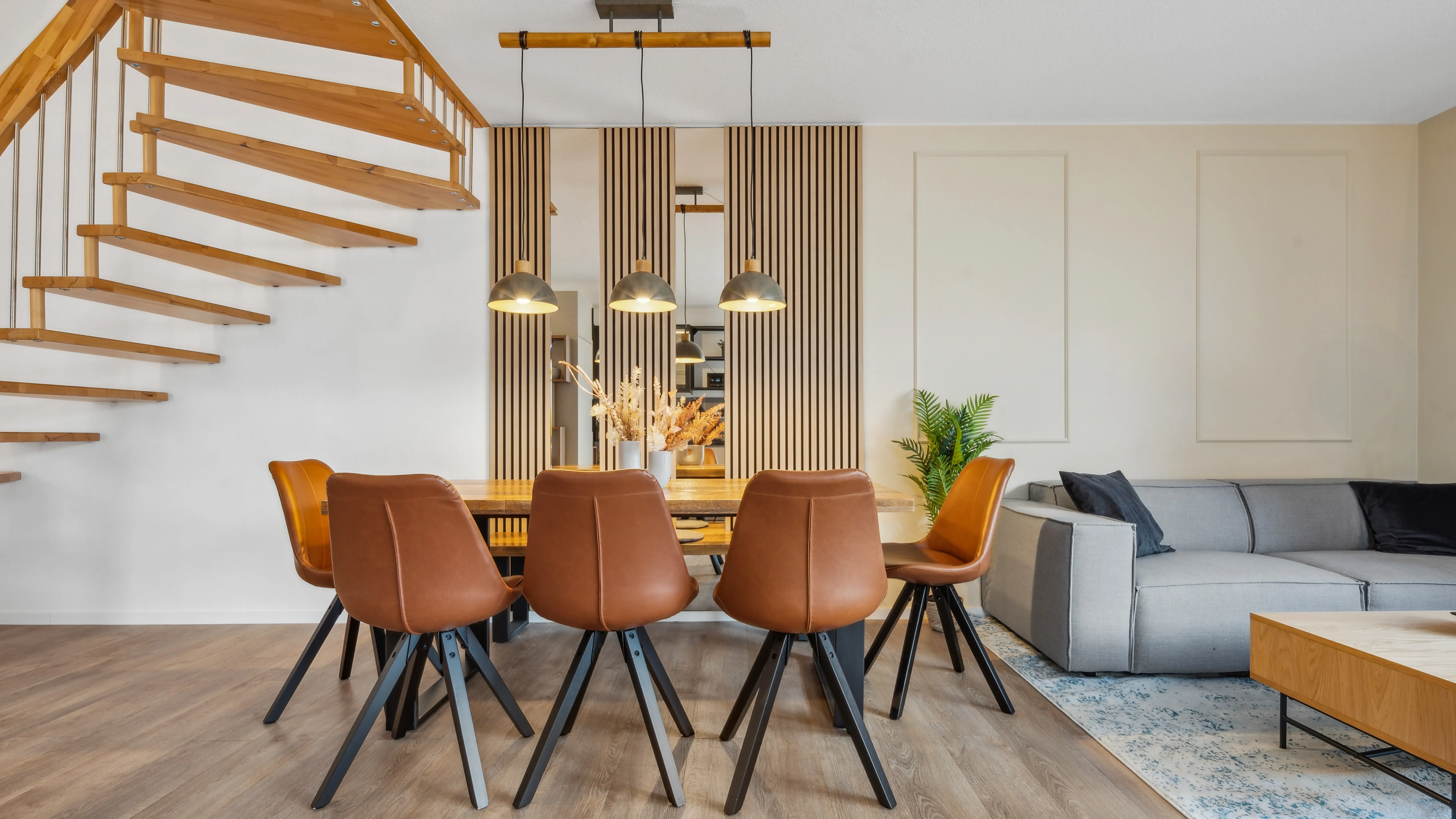 Heller Essbereich mit großem Holztisch, Lederstühlen, Hängeleuchten und offener Holztreppe