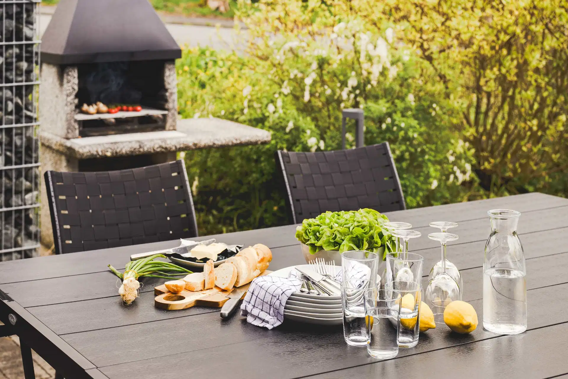 Gedeckter Gartentisch mit Steingrill im Hintergrund