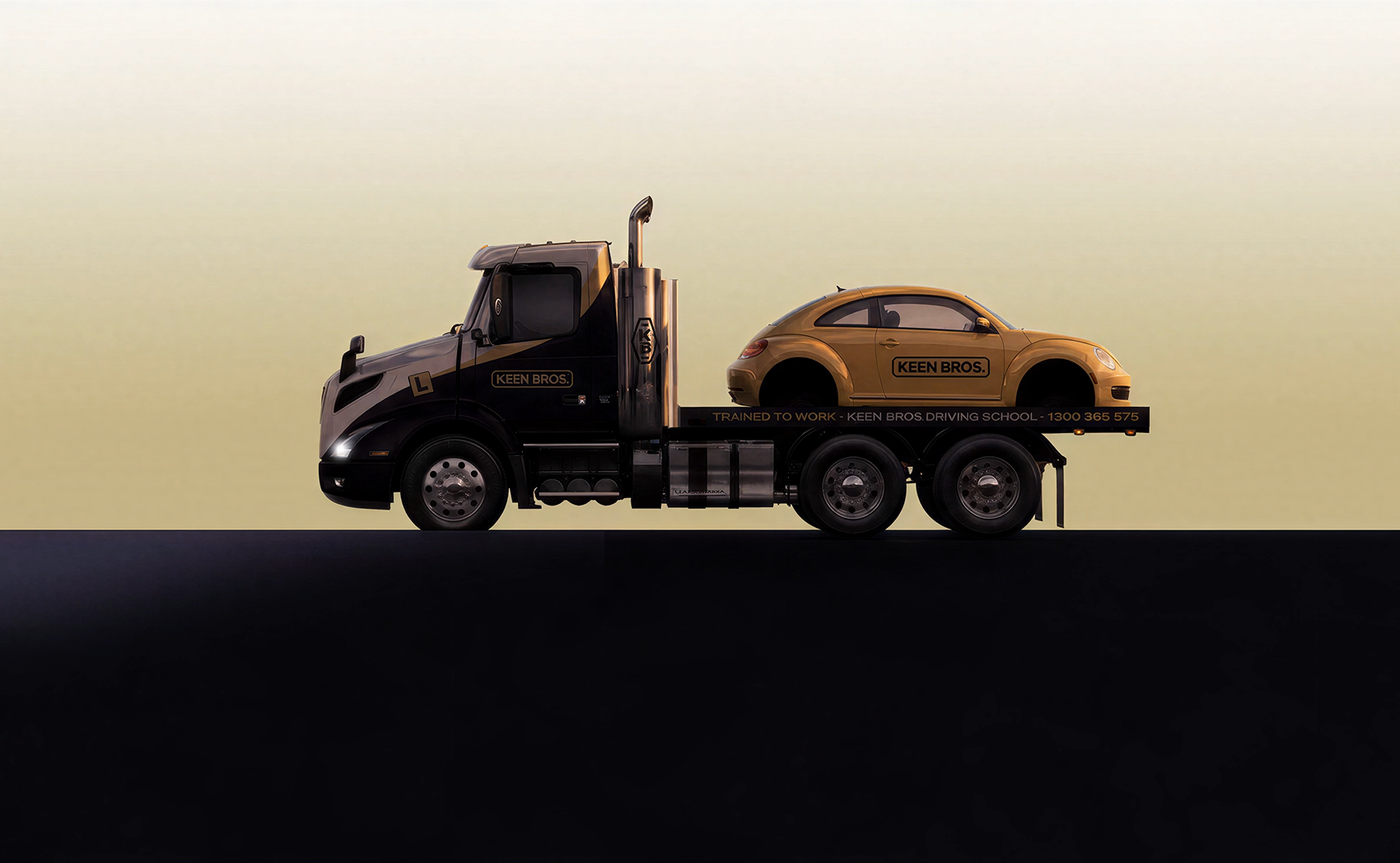 Side profile of a black and gold tow truck with 'Keen Bros.' branding carrying a gold Volkswagen Beetle also branded with 'Keen Bros.' on a flatbed against a beige background.