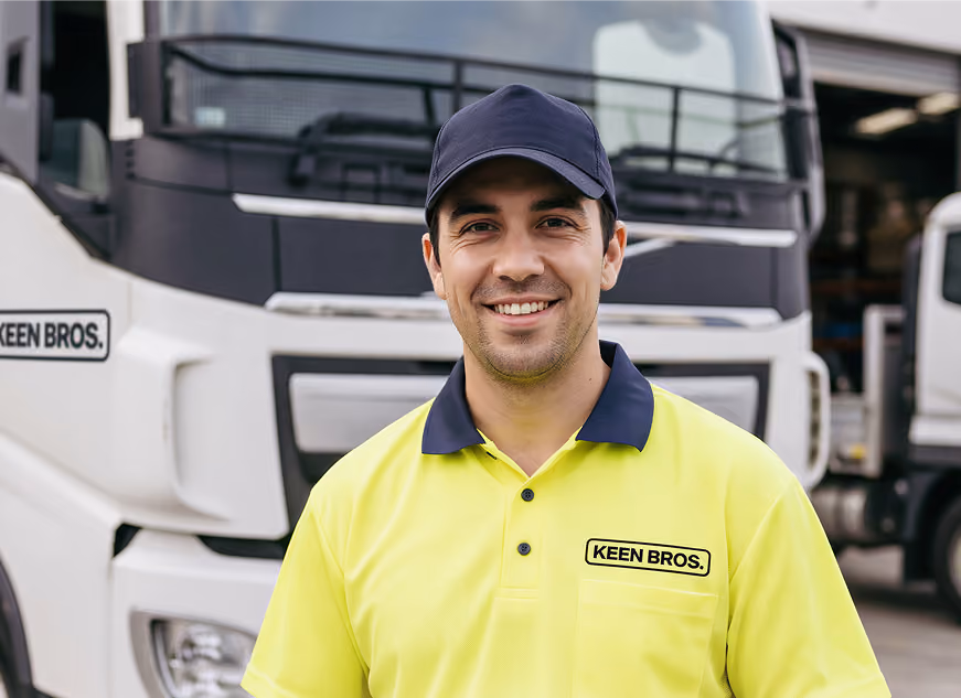 Smiling man wearing a black cap and a yellow polo shirt with a 'KEEN BROS.' logo standing in front of a white truck.