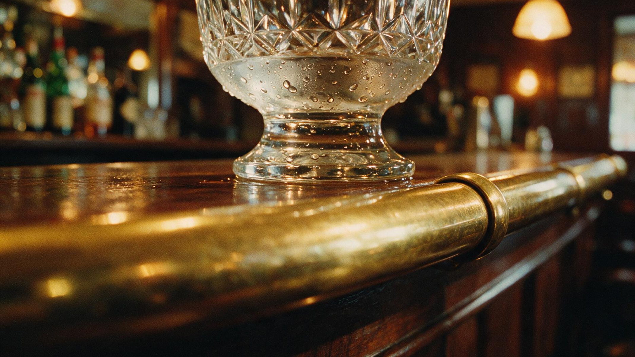 Verre de cristal posé sur un comptoir de bar en laiton, lumière ambrée