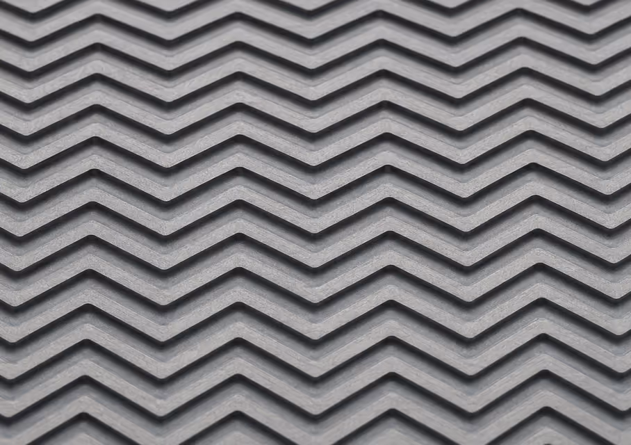 Close-up of a textured surface with a repeating chevron or zigzag pattern in gray, creating a 3D effect with shadows in the grooves.