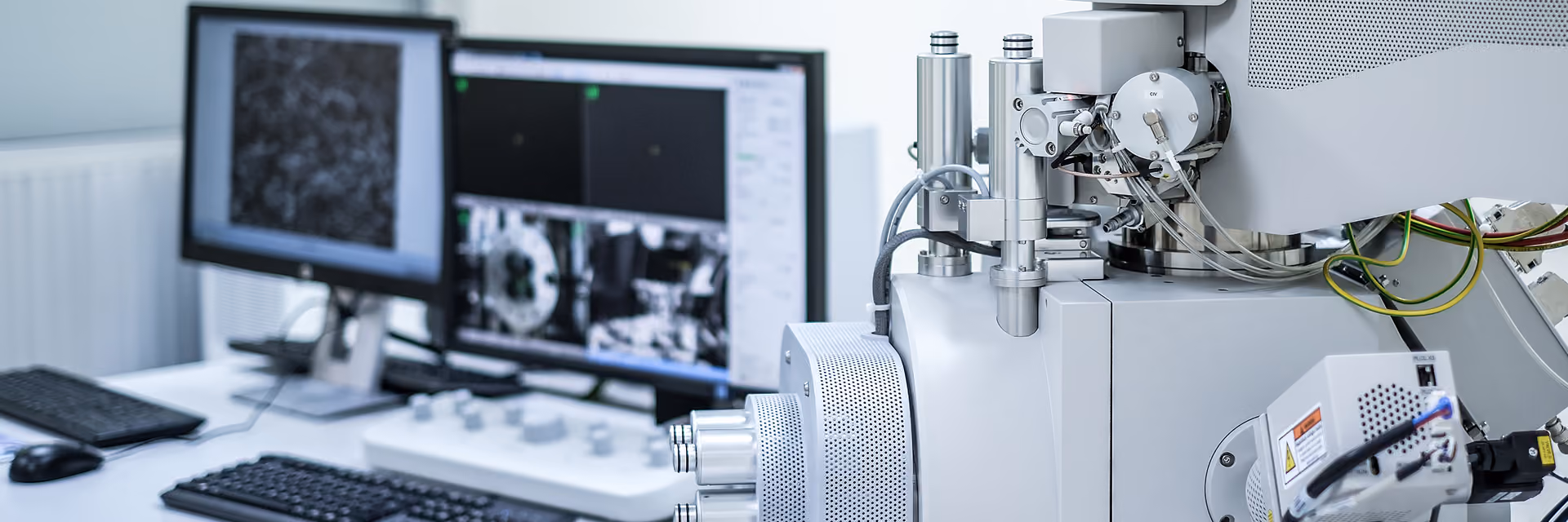 Close-up of a scientific electron microscope with dual monitors displaying magnified images and data, used for detailed material analysis in a laboratory.