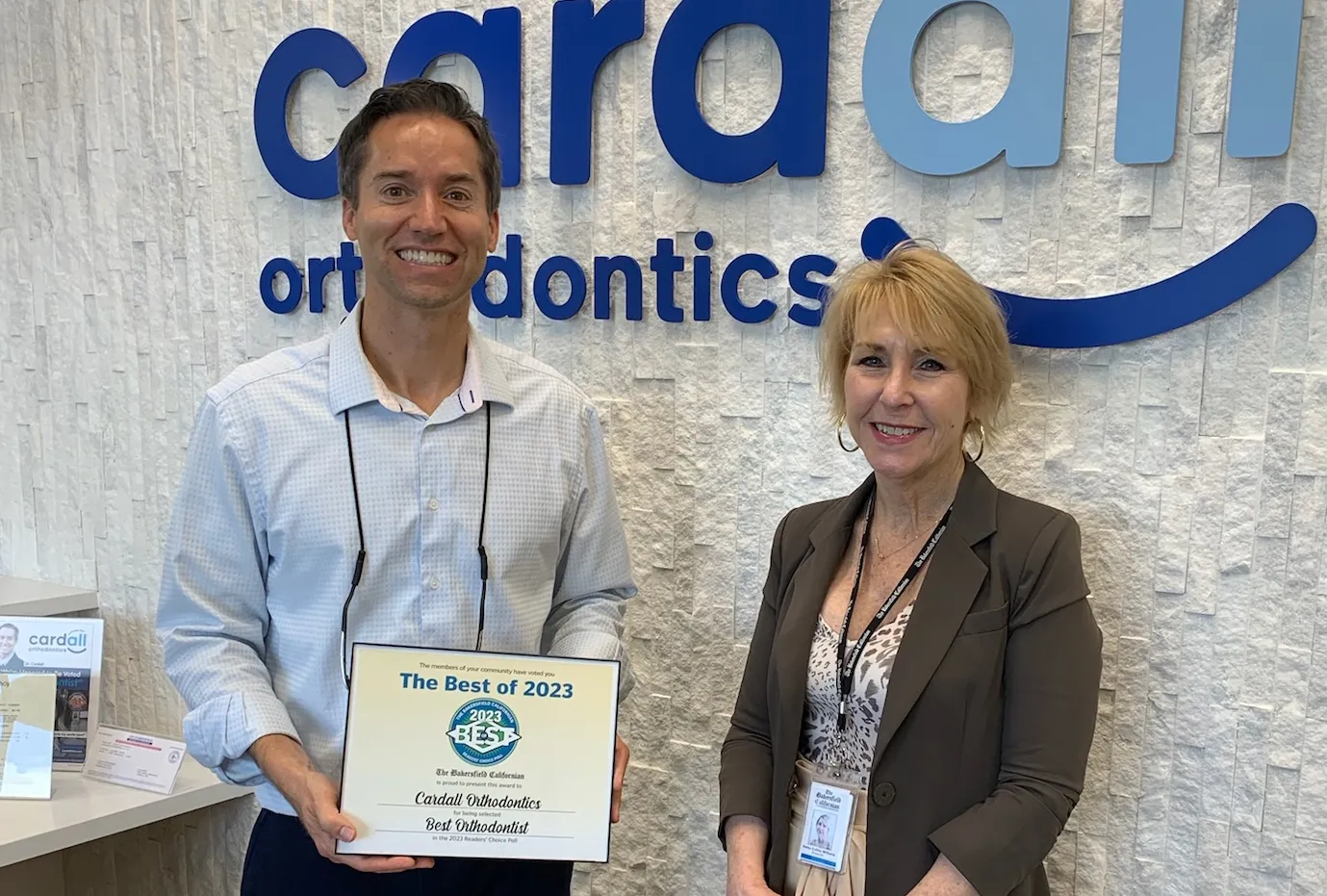 Smiling orthodontist and colleague pose beneath a “cardall orthodontics” sign, holding a 2023 award for clinical excellence.