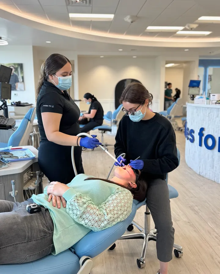 Masked dental professionals in blue gloves use dental tools to treat a reclining patient in a bright clinic, creating a calm, clinical atmosphere.