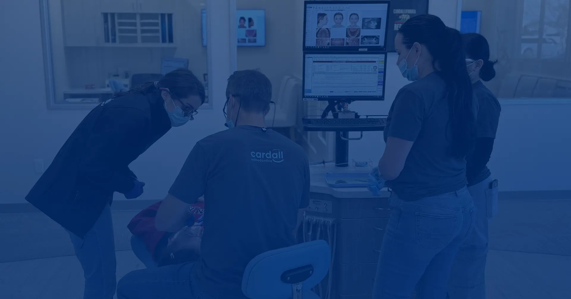 Medical team in a hospital room gathers around a seated patient and monitors, suggesting a focused, collaborative healthcare consultation.