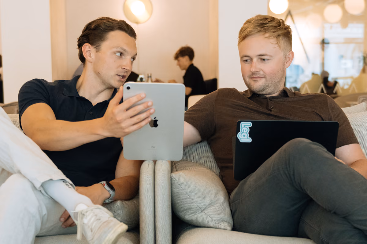 Two colleagues on a sofa reviewing content on an iPad and a laptop with a Legl sticker