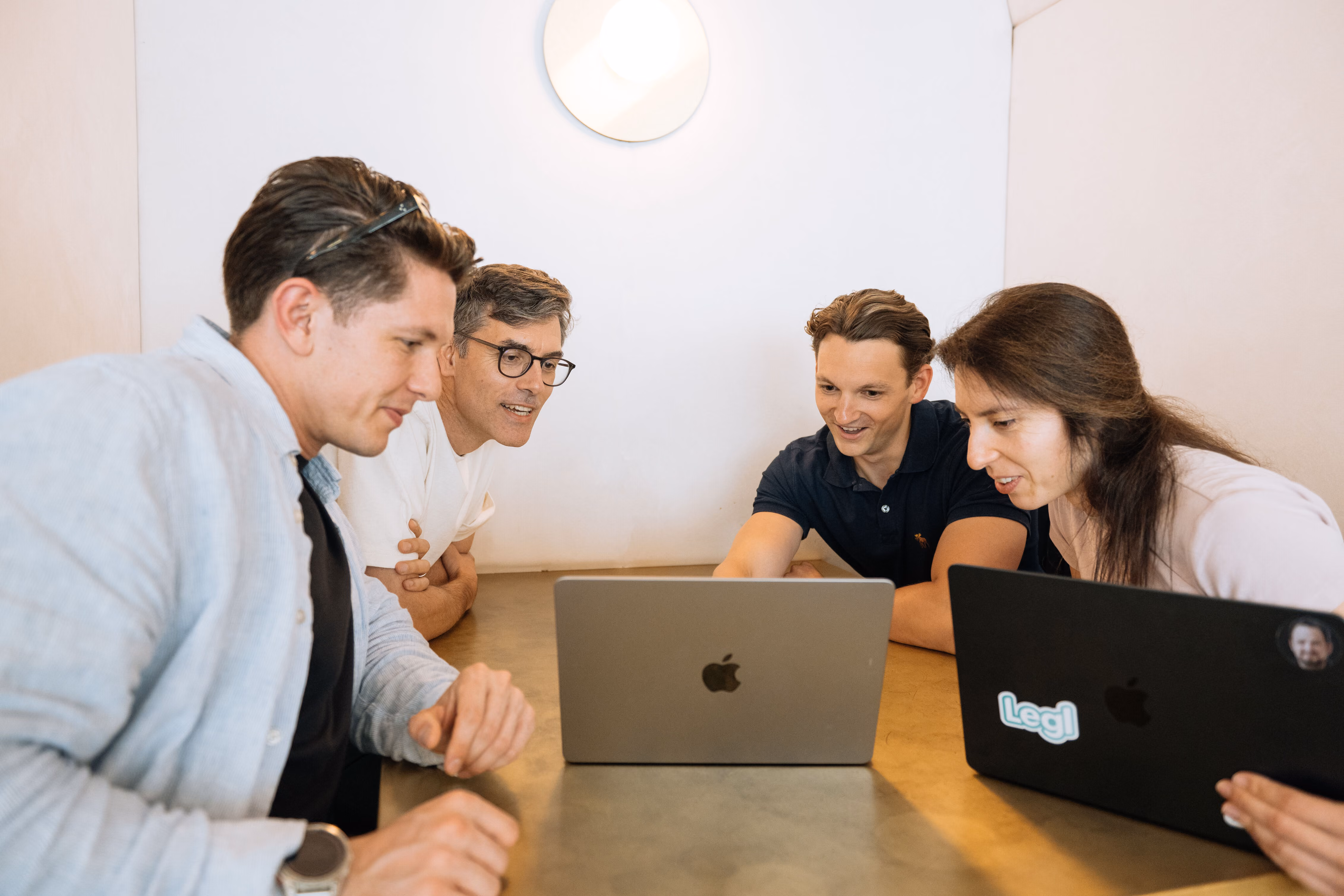 Four colleagues looking and smiling at two laptops during a meeting at a table.